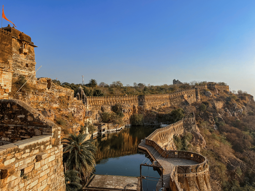 Elevated pathway at Chittorgarh Fort, India’s largest fort, overlooking valley and water body, with stone railings and steep cliffs, offering sweeping views of surrounding rugged landscape