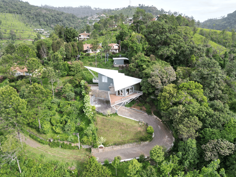 Elevated view of a house set against forested hills under a cloudy sky at Ibex Resorts, Coonoor (Tapas).