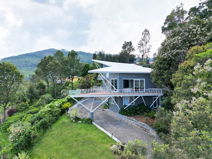 An aerial view of a modern grey resort villa with a white roof and a spacious balcony, nestled amidst lush greenery and hills - Ibex Resorts, Coonoor (Tapas)