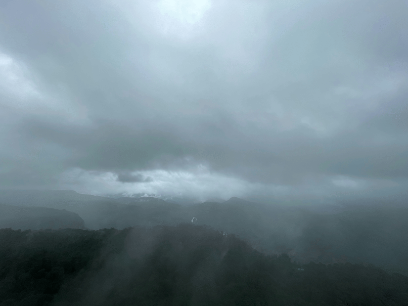 A view of Anamalai HIlls in the Western Ghats with mist covering the entire area and dark clouds above.