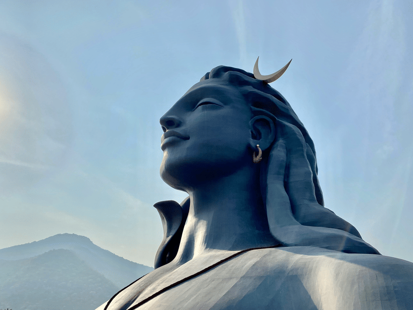 A side-profile view of the Adiyogi statue with mountains in the background.
