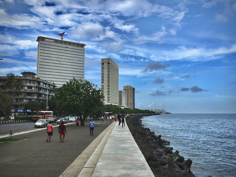 An overview of the Marine Drive with people walking on the sidewalk next to the Arabian Sea. Marine Drive is one of the must-visit place on your things to do in Mumbai during monsoons.