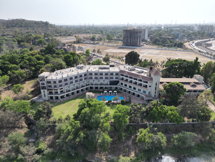 An aerial view of a large resort with a swimming pool in front, surrounded by dense greenery beneath a clear sky at VITS Kamats Resort, Silvassa