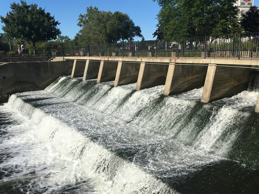 a small dam with water flowing from the crevices with trees in the background 