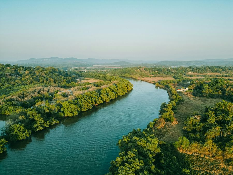 A meandering river cuts through a verdant landscape with dense trees and distant hills under a clear sky.