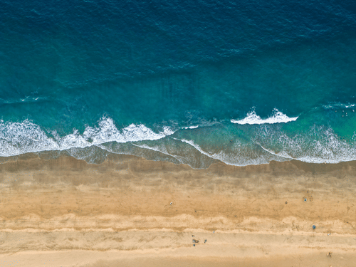 A top-down aerial view of Agonda Beach with the blue0green waves crashing on the shoreline.
