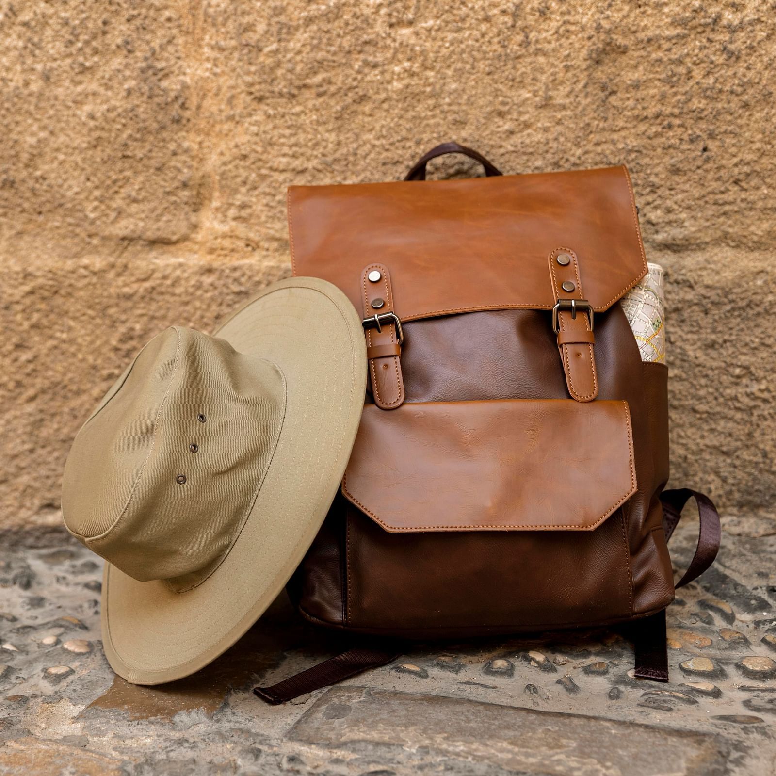 Safari backpack and wide-brimmed hat resting against a textured stone wall, ready for an outdoor adventure