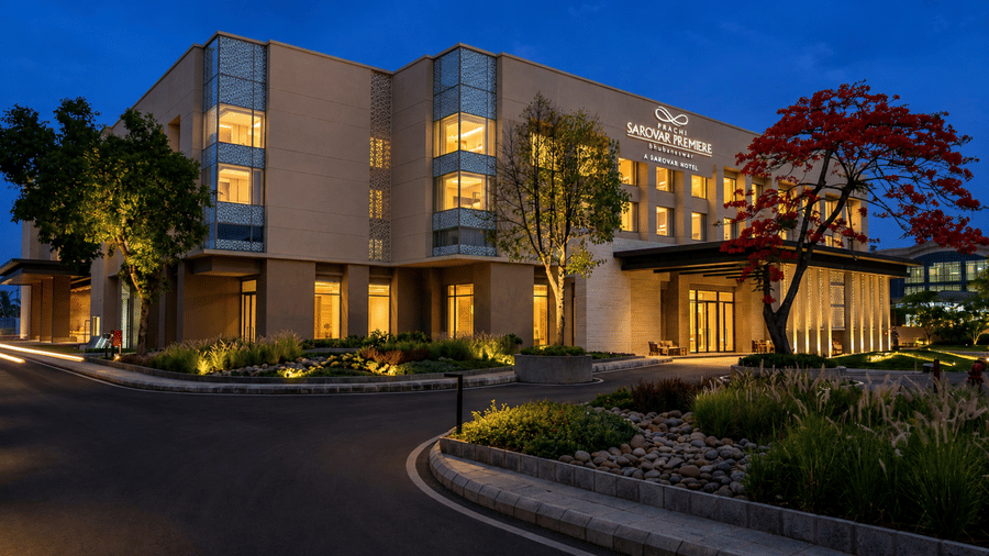 Exterior & multi-storey facade of Prachi Sarovar Premiere hotel in Bhubaneswar seen under dark sky with well-lit interiors, and a driveway with manicured plants on either sides.