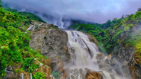 A scenic waterfall cascading down the rocky cliffs of Cherrapunji, Meghalaya, surrounded by dense green vegetation.