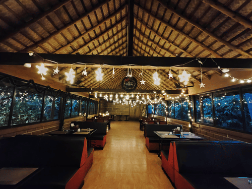 An indoor restaurant or lounge area at night, characterized by a high, textured ceiling, rows of booth seating, and numerous string lights strung across the space, creating a warm ambiance.
