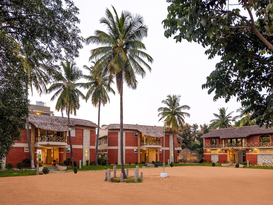 Resort exterior view looking across a dusty courtyard toward multi-story red-brick buildings and palm trees