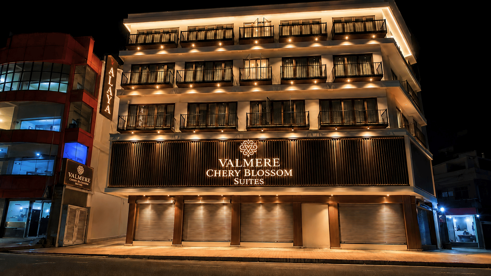 A 4-storey building of Valmere Chery Blossom Suites, illuminated at night with a sign board reflecting the signage of the hotel.