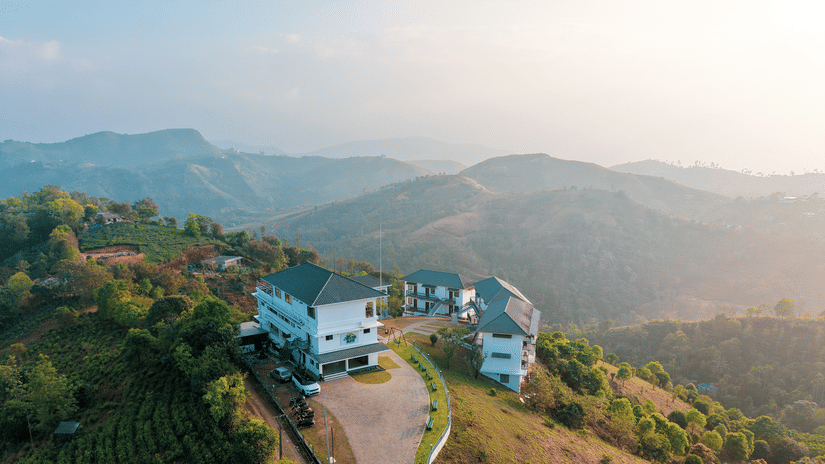 An aerial view of Abad Silver Mist, Vagamon, the best family resorts in Vagamon, on a grassy hilltop surrounded by tea plantations and rolling mountains