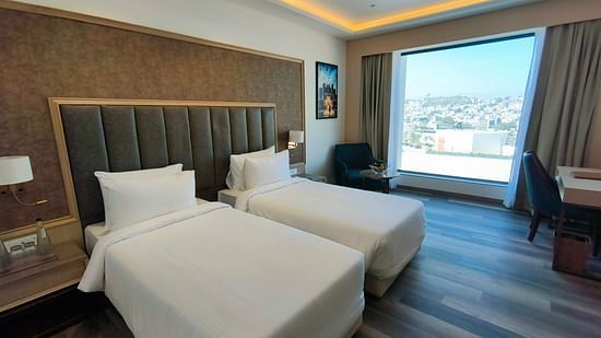 A hotel room in Ajmer with a twin bed setup, stylish furniture, and ample natural light - Sarovar Portico, Ajmer