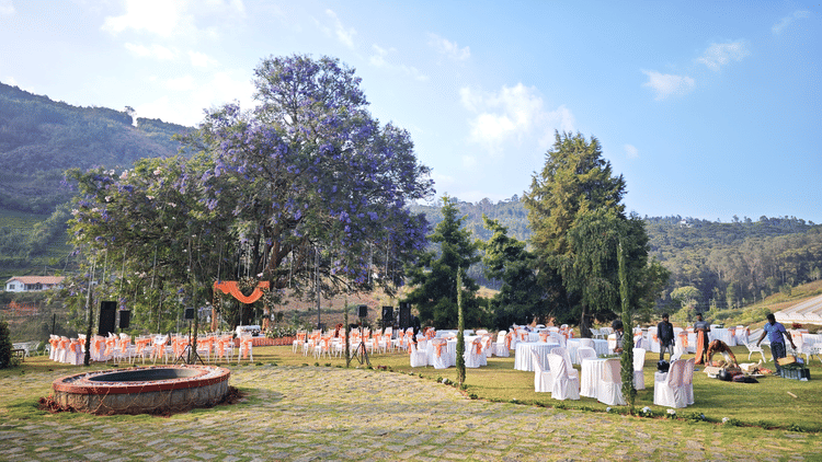  Scenic view of an outdoor wedding venue during the day with guests, chairs, and an altar under a blooming purple-flowered tree in Coonoor - Ibex Resorts, Coonoor (Leewood).