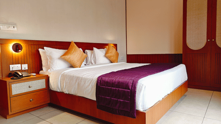 A neatly made double bed at Bliss Giriya By Bergamont Tiruvannamalai with a wooden headboard and wall-mounted reading lights.