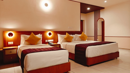 A triple-bedded room at Bliss Giriya By Bergamont Tiruvannamalai with wooden headboards and wall-mounted reading lights.