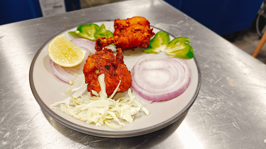 2 pieces of fried chicken accompanied by sliced red onions, shredded cabbage, capsicum, and a lemon wedge at Bliss Casa Mila By Bergamont Hotels, Kodaikanal.