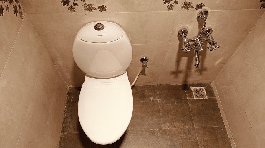 A white ceramic toilet located next to chrome taps in a bathroom with decorative leaf-patterned tiles at Bliss Casa Mila By Bergamont Hotels, Kodaikanal.