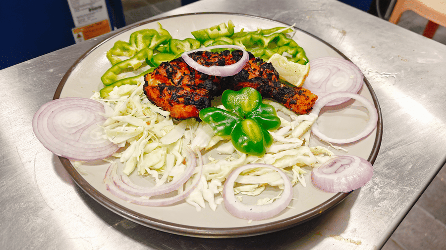 A grilled chicken piece served with sliced red onions, shredded cabbage, green chillies, and a lemon wedge at Bliss Casa Mila By Bergamont Hotels, Kodaikanal.