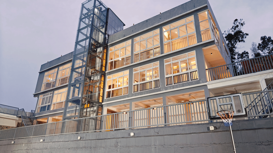 A modern 4-storey building with large glass windows and an external lift shaft at dusk at Bliss Casa Mila By Bergamont Hotels, Kodaikanal.