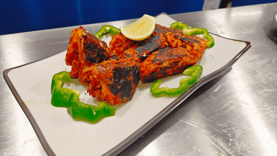 Pieces of tandoori fish garnished with green capsicum rings and a lemon wedge on a rectangular plate at Bliss Casa Mila By Bergamont Hotels, Kodaikanal.