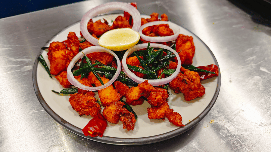 Fried chicken pieces served on a plate with red onion rings, green chillies, and a lemon wedge at Bliss Casa Mila By Bergamont Hotels, Kodaikanal.