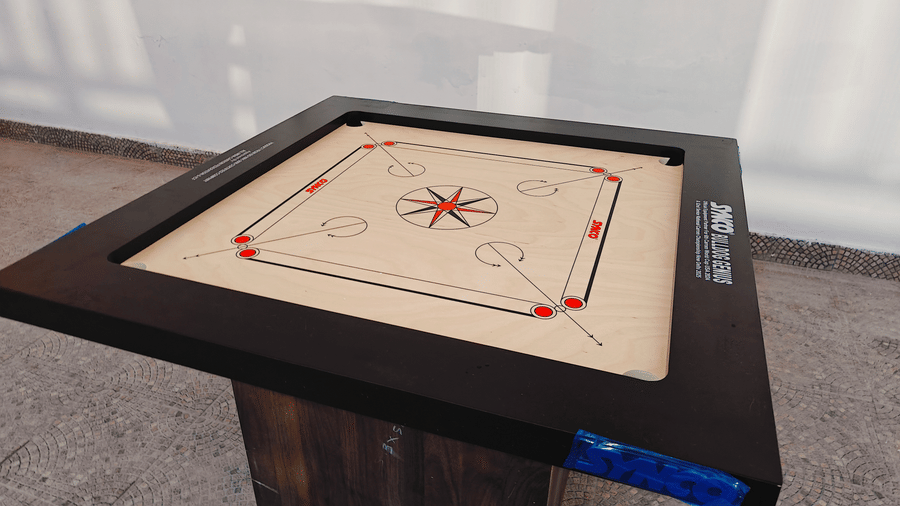 A wooden carom board with red and white pieces sits on a stand in an indoor area at Bliss Casa Mila By Bergamont Hotels, Kodaikanal.