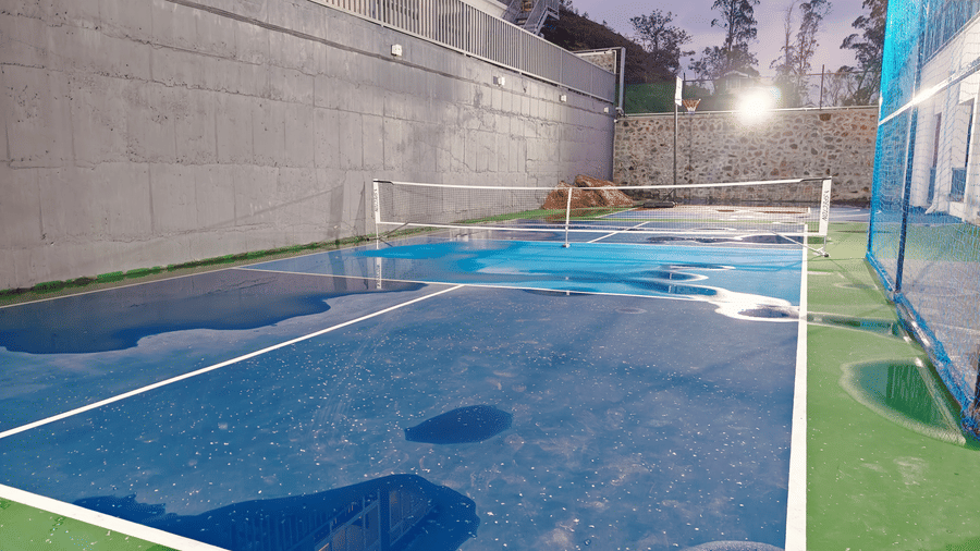 A blue and green outdoor court with a white net sits next to a grey concrete wall at Bliss Casa Mila By Bergamont Hotels, Kodaikanal.