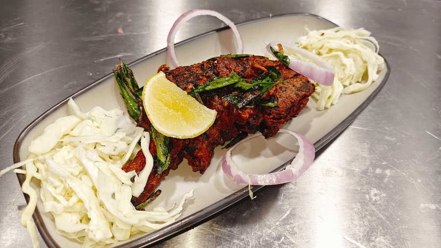 A portion of roasted meat garnished with fresh green herbs, shredded cabbage, and red onion rings at Bliss Casa Mila By Bergamont Hotels, Kodaikanal.