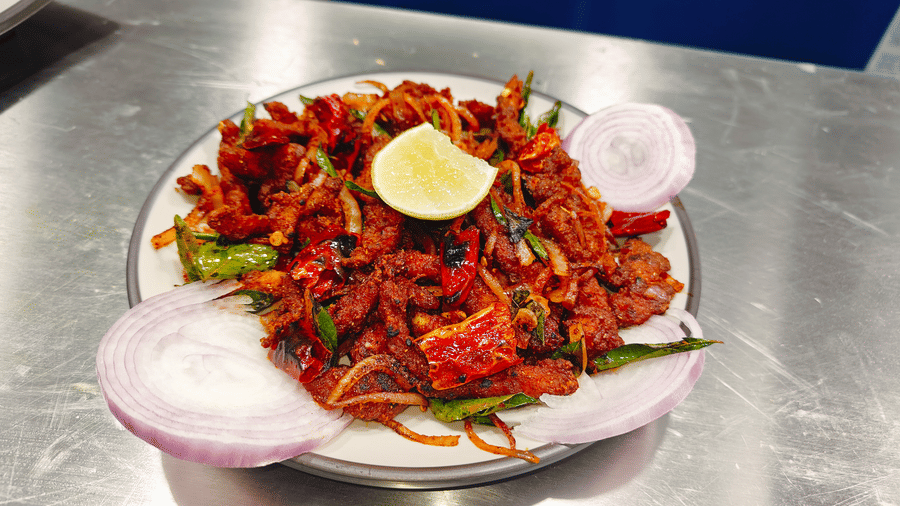 A plate of reddish-brown sautéed meat mixed with sliced onions and green chillies, topped with a lemon wedge at Bliss Casa Mila By Bergamont Hotels, Kodaikanal.