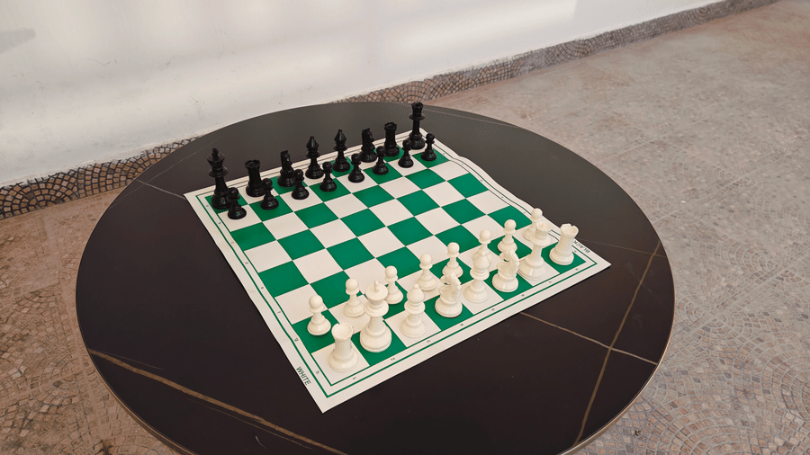 A green and white chessboard with black and white pieces arranged on a round dark table at Bliss Casa Mila By Bergamont Hotels, Kodaikanal.