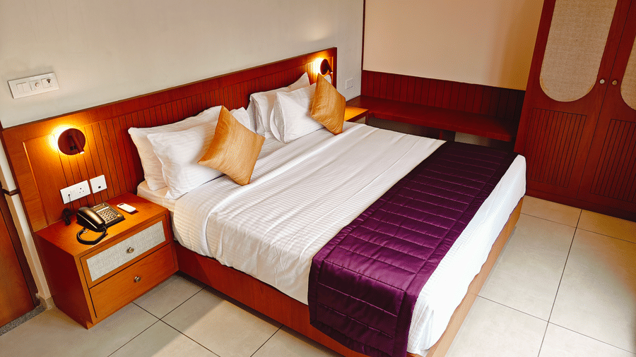 A neatly made double bed at Bliss Giriya By Bergamont Tiruvannamalai with a wooden headboard and warm wall lighting.