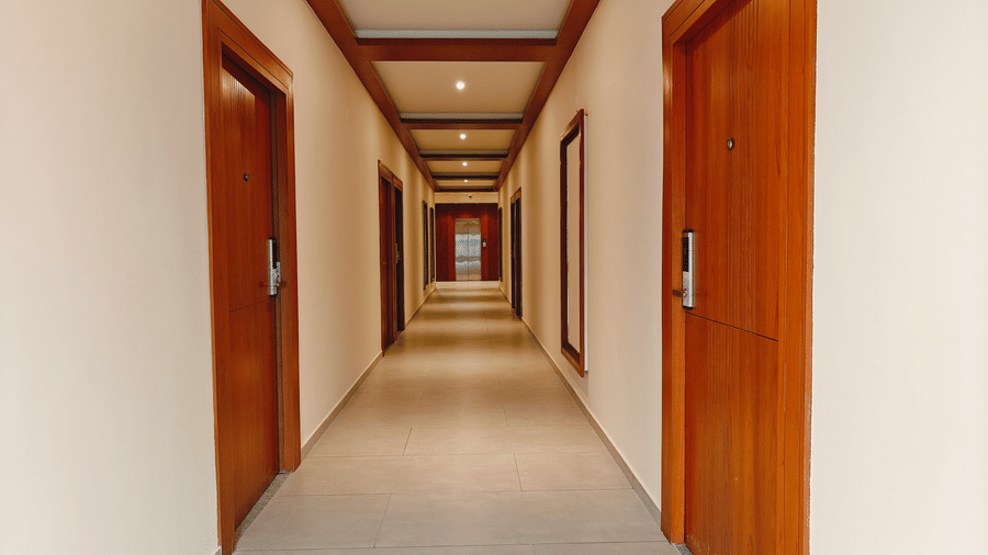 A well-lit hotel corridor at Bliss Giriya By Bergamont Tiruvannamalai with wooden doors and recessed ceiling lighting.