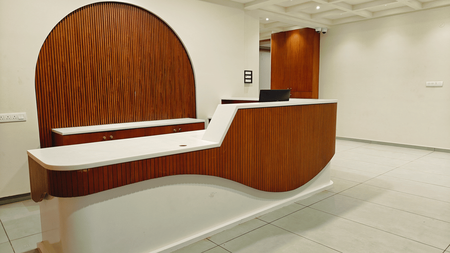 A curved wooden reception desk at the front lobby of Bliss Giriya By Bergamont Tiruvannamalai.