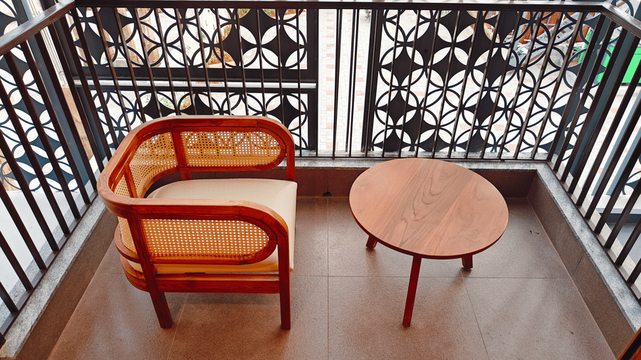 A private balcony at Bliss Giriya By Bergamont Tiruvannamalai with wicker seating, a side table, and latticed railings.