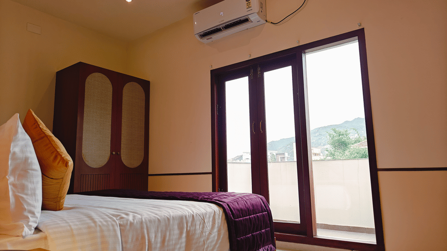 A room at Bliss Giriya By Bergamont Tiruvannamalai with a double bed, wardrobe, and large French windows opening to a balcony.