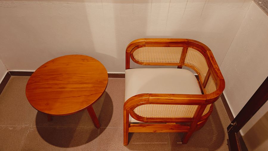 A wooden armchair and round side table in a room at Bliss Giriya By Bergamont Tiruvannamalai.