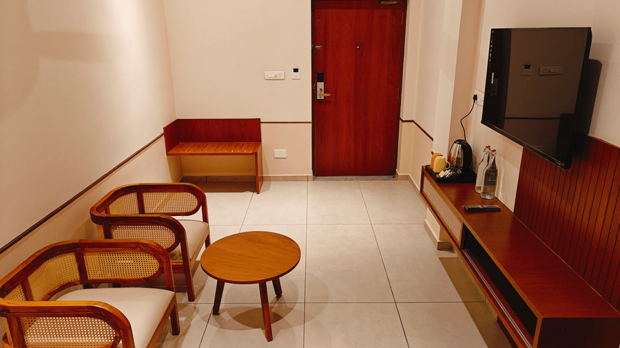 A room sitting area at Bliss Giriya By Bergamont Tiruvannamalai with wicker chairs, a round table, and a wall-mounted television.