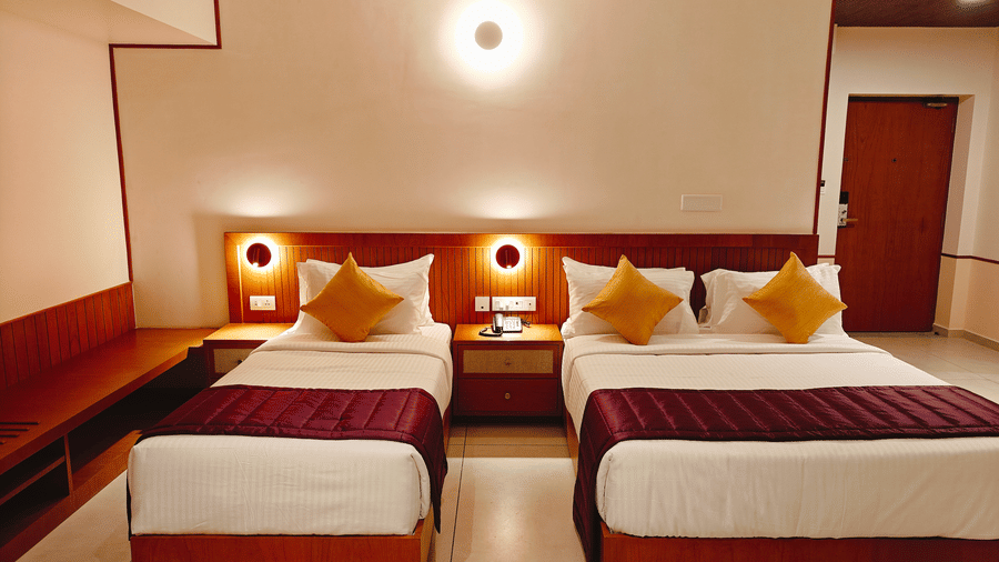 A twin-bedded room at Bliss Giriya By Bergamont Tiruvannamalai with wooden headboards and warm ceiling lighting.