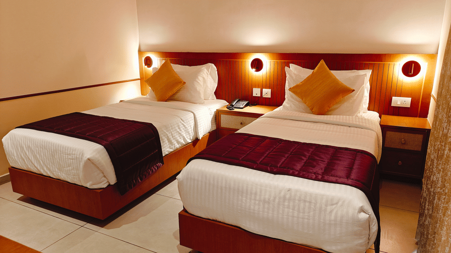 A close view of twin beds at Bliss Giriya By Bergamont Tiruvannamalai with wooden headboards and wall-mounted reading lights.