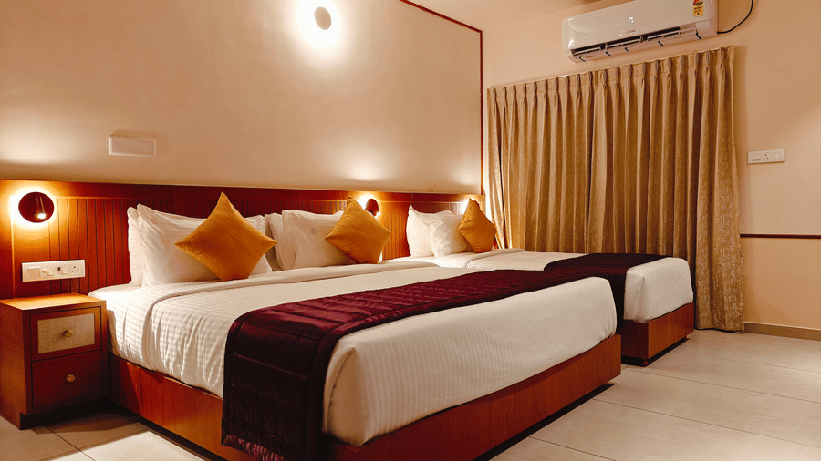 A twin-bedded room at Bliss Giriya By Bergamont Tiruvannamalai with wooden headboards, reading lights, and floor-length curtains.