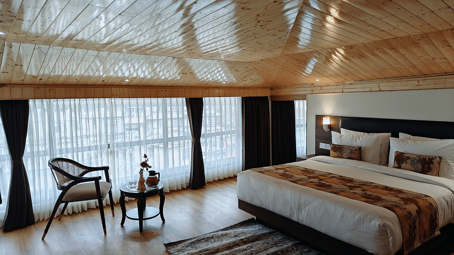 A hotel room featuring a neatly made bed with white linens and a patterned runner, accompanied by a chair and a small table beside it - Sumitel JB Park, Darjeeling