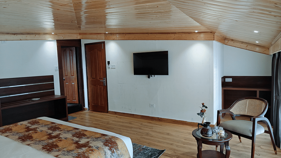 A hotel room with a bed, a chair and a tv mounted on the wall with a warm lighting - Sumitel JB Park, Darjeeling