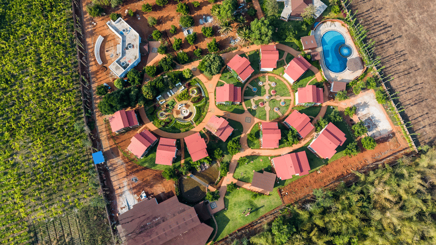 w (18)aAn aerial view of a resort layout featuring red-roofed cottages arranged in a semi-circle with a swimming pool and lawns | Lords Sahyadri Resort, Shivamogga