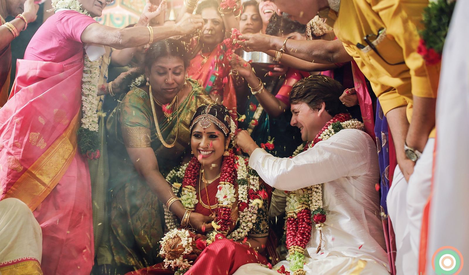 A traditional Indian wedding scene with the bride and groom surrounded by vibrant colours and floral decorations.