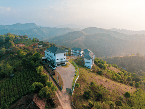 An aerial view of Abad Silvermist, Vagamon, the best family resorts in Vagamon, on a grassy hilltop surrounded by tea plantations and rolling mountains