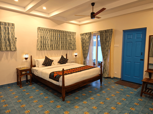  A well-appointed bedroom with a large bed, wooden frame, and colorful throw, complemented by a blue tiled floor, a blue door, and patterned curtains.