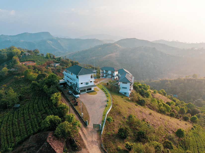 An aerial view of Abad Silvermist, Vagamon, the best family resorts in Vagamon, on a grassy hilltop surrounded by tea plantations and rolling mountains