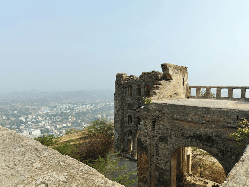 Chittorgarh Fort with arched opening overlooking expansive townscape below, weathered stone surfaces and elevated position